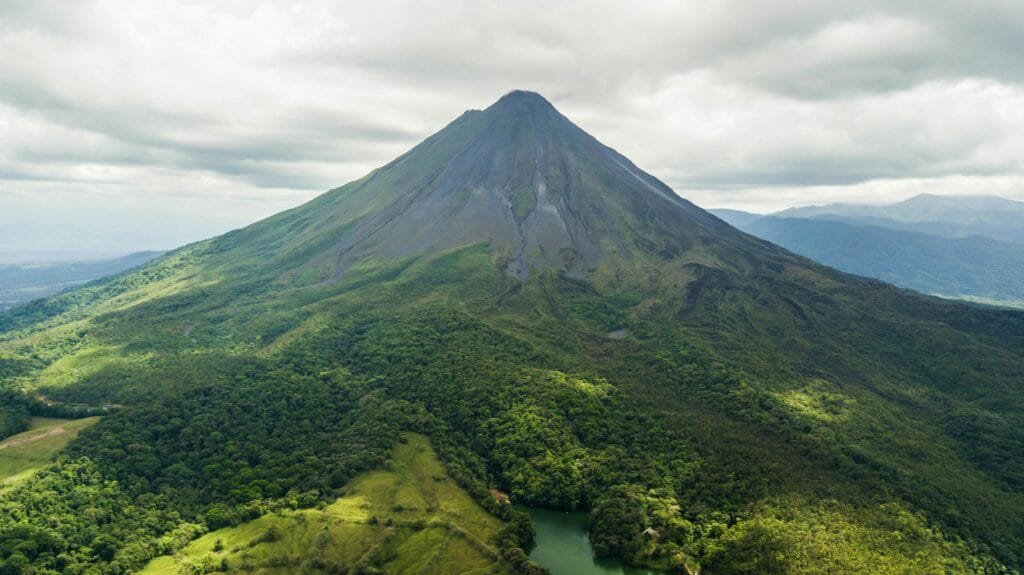 Dramatic aerial view of the lush green Arenal Volcano in Costa Rica against a cloudy sky.